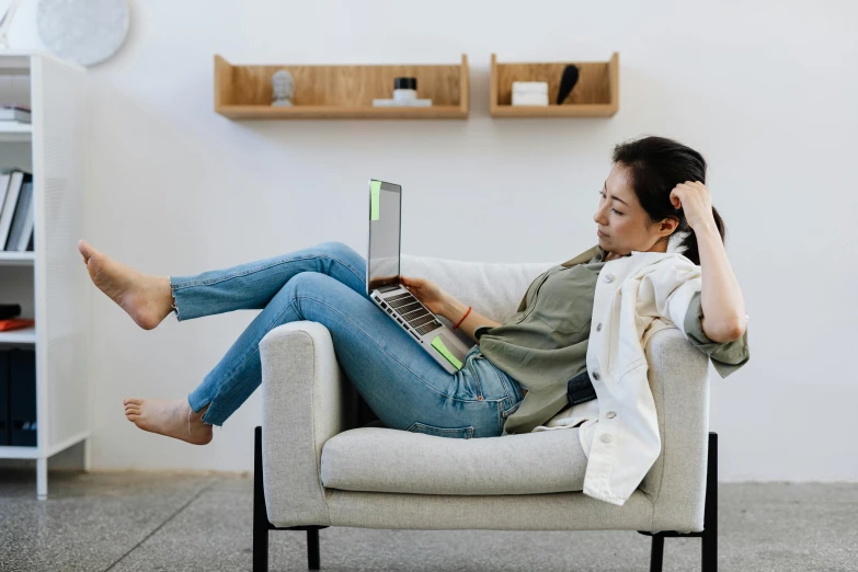 a woman sitting in a chair with a laptop, trending on pexels, happening, laying down, smart casual, open plan, old couch