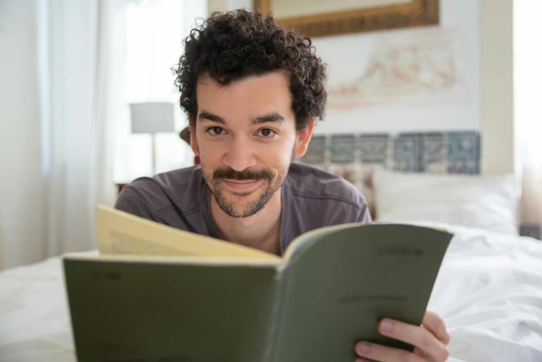 a man reading a book on a bed, by Simon Marmion, nathan fielder, mixed race, fan favorite, profile image