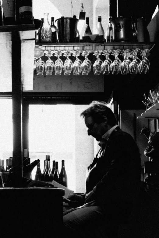 a black and white photo of a man sitting at a bar, inspired by Louis Stettner, fluxus, bottles, in profile, setting sun, ffffound