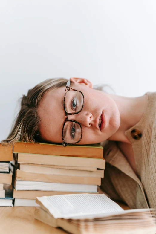 a woman laying on top of a pile of books, trending on pexels, square rimmed glasses, disappointed, sydney sweeney, chemistry