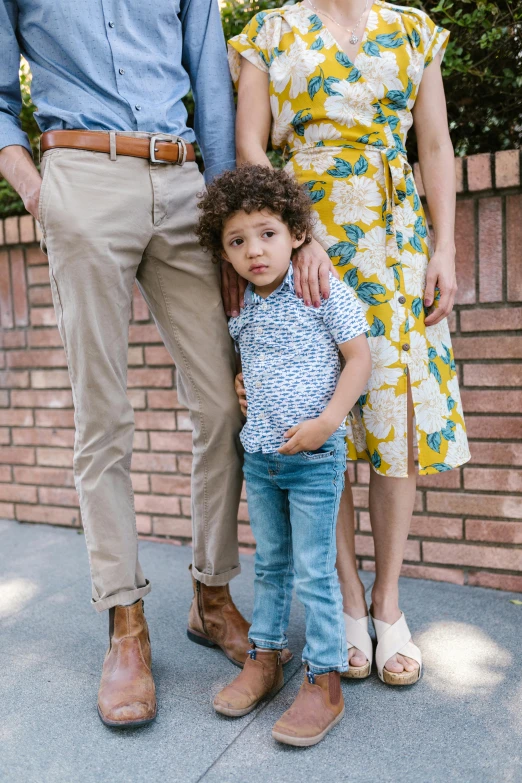 a family poses for a picture in front of a brick wall, legs intertwined, full body hero, ad image, little boy