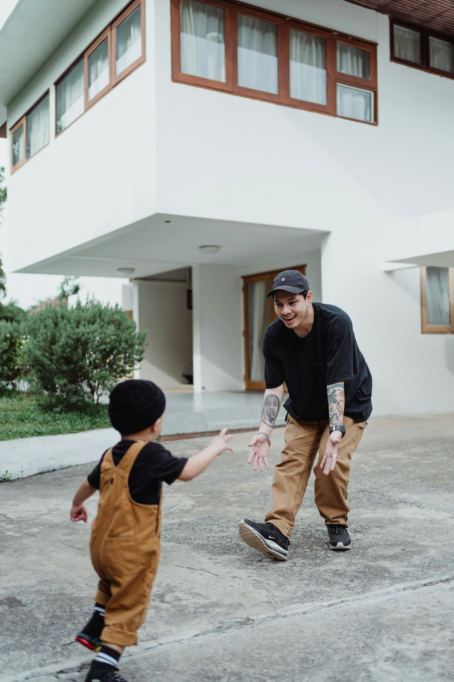 a man holding a child's hand in front of a house, by Robbie Trevino, pexels contest winner, skateboarder style, smiling playfully, thawan duchanee, slightly minimal