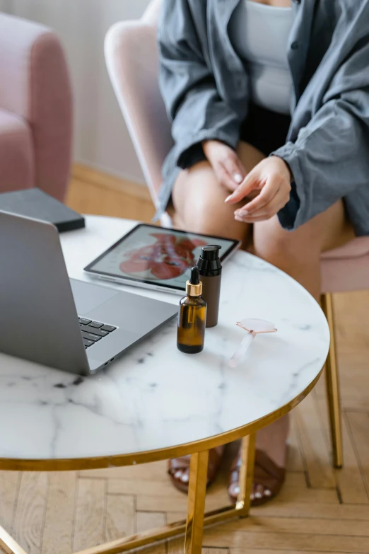 a woman sitting at a table with a laptop, by Julia Pishtar, trending on pexels, happening, vials, skincare, full-body, oils
