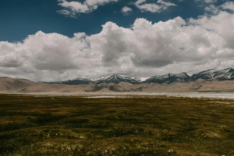 the clouds are in the sky over a field and mountains