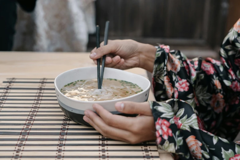 a person holding a bowl of noodles on a table