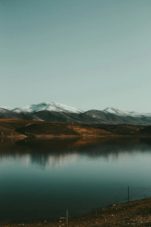 a lake is next to a hilly area with mountains in the background