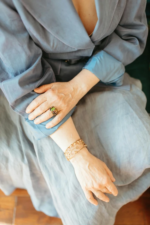 a woman in a blue dress sitting on a chair, inspired by Marià Fortuny, trending on pexels, renaissance, brass bracelets, green and brown clothes, swollen veins, detail shot