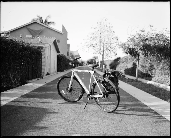 a bicycle parked on the side of a road, a black and white photo, walking through a suburb, bay area, shot with a arriflex 35 ii, with a long white
