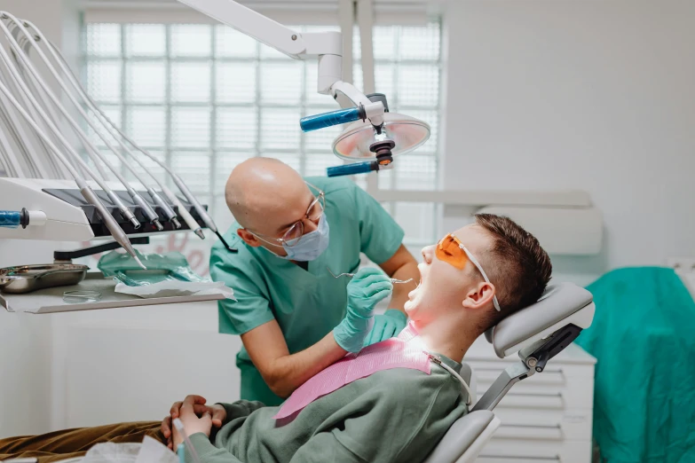a man sitting in a chair next to a woman in a dentist's chair, by Adam Marczyński, pexels contest winner, hurufiyya, square masculine jaw, with electric arc device, sydney hanson, acid leaking from mouth