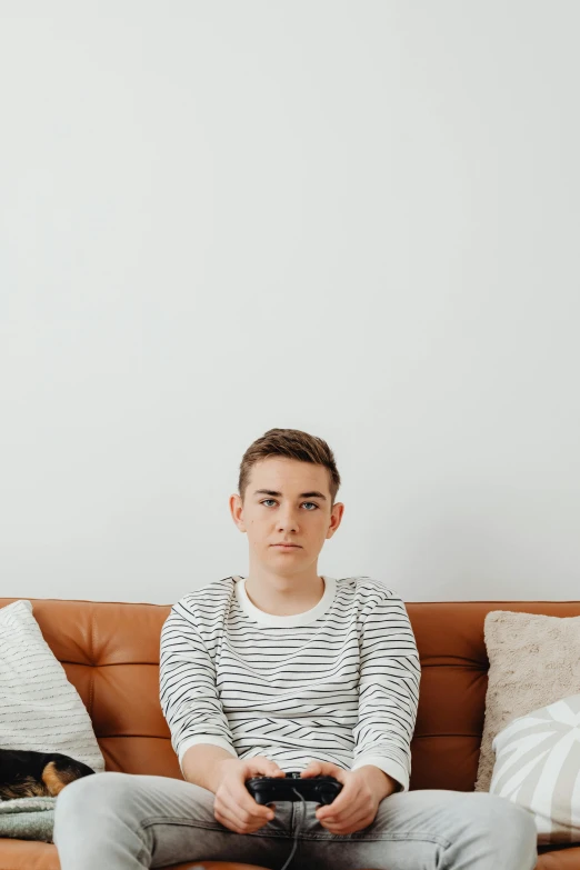 a man sitting on a couch holding a video game controller, an album cover, by Carey Morris, trending on pexels, minimalism, portrait androgynous girl, wearing stripe shirt, disappointed, julian ope