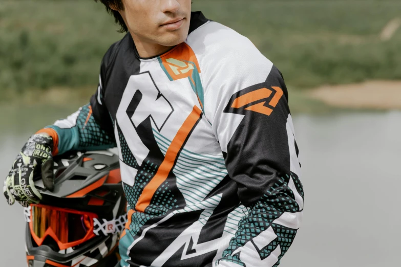 a young man standing next to a body of water, motocross bike, federation clothing, teal and orange, zoomed in shots