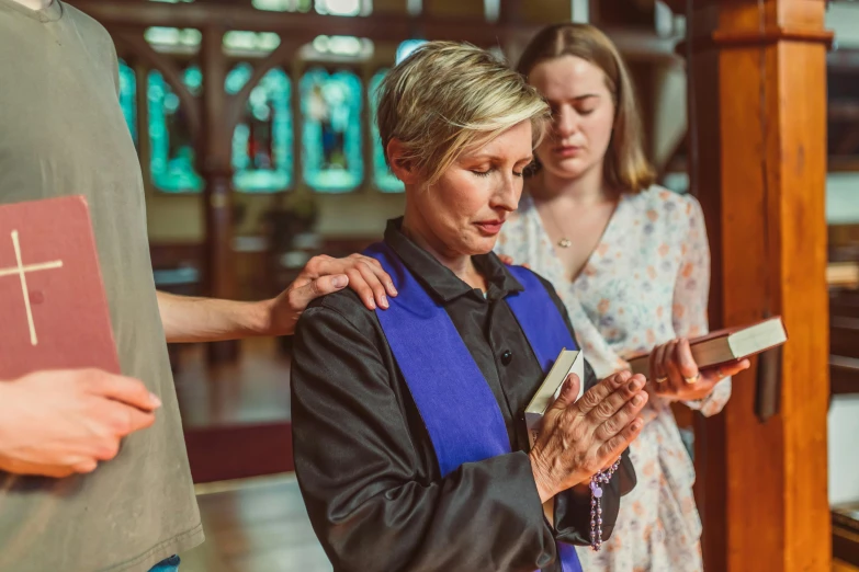 a woman standing next to a man holding a bible, a photo, pexels, renaissance, scene set in a church, blue tunic and robes, woman holding another woman, wearing headmistress uniform