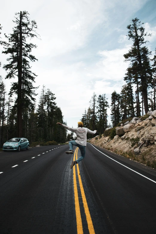 someone skate boarding down a road near some pine trees