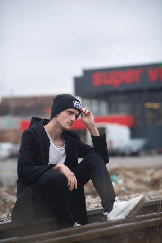 a man sitting on a train track talking on a cell phone, by Jacob Toorenvliet, unsplash, superflat, with black beanie on head, jamie campbell bower, standing in a township street, profile posing