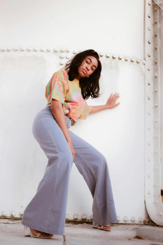 a woman standing in front of a white wall, a colorized photo, by Dulah Marie Evans, trending on pexels, sza, sitting on top a table, pastel clothing, flares