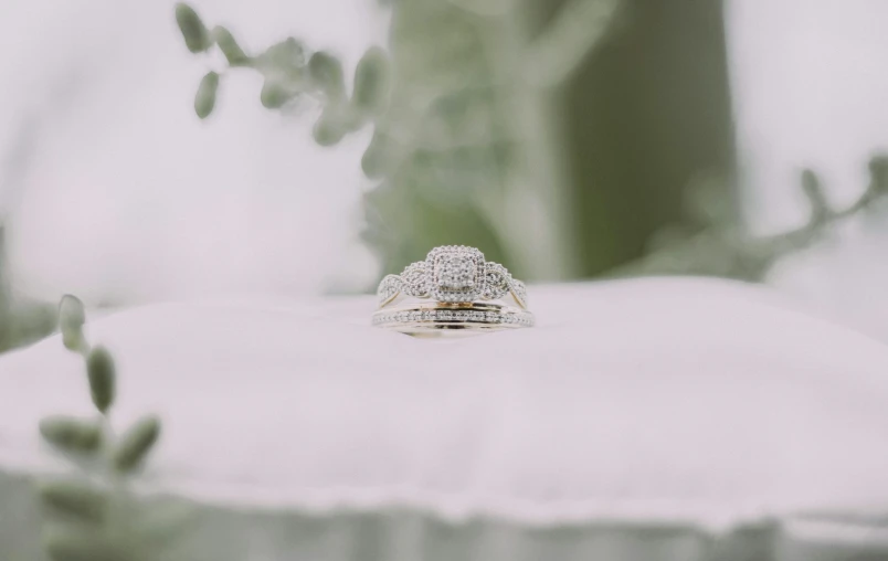 a diamond ring sitting on top of a white pillow, by Emma Andijewska, pexels, fan favorite, gold and green, [ cinematic, stacked