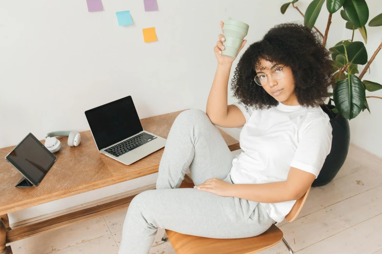 a woman sitting on a chair holding a cup, trending on pexels, happening, curly haired, with a laptop on his lap, olive skinned, various pose