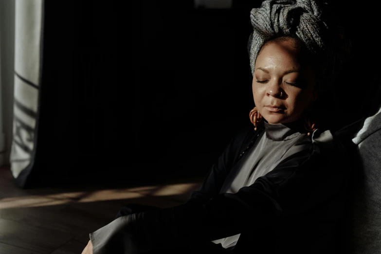 a woman sitting on a couch with her eyes closed, a portrait, inspired by Carrie Mae Weems, pexels contest winner, wrapped in a black scarf, light glare, meditating pose, slide show