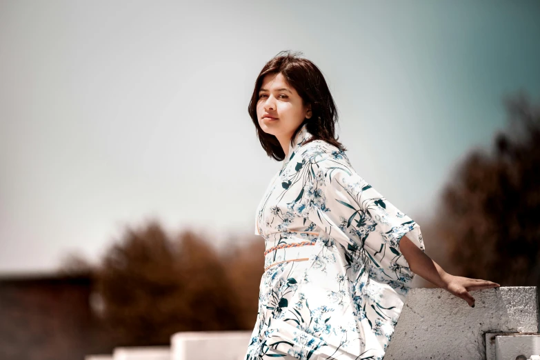 a woman poses near a cement wall, in the outdoors