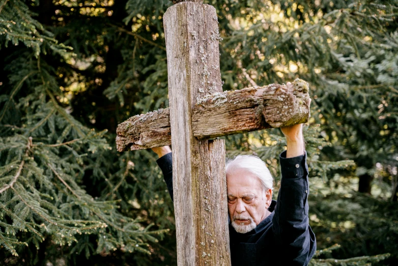 a man holding onto a wooden cross in the woods