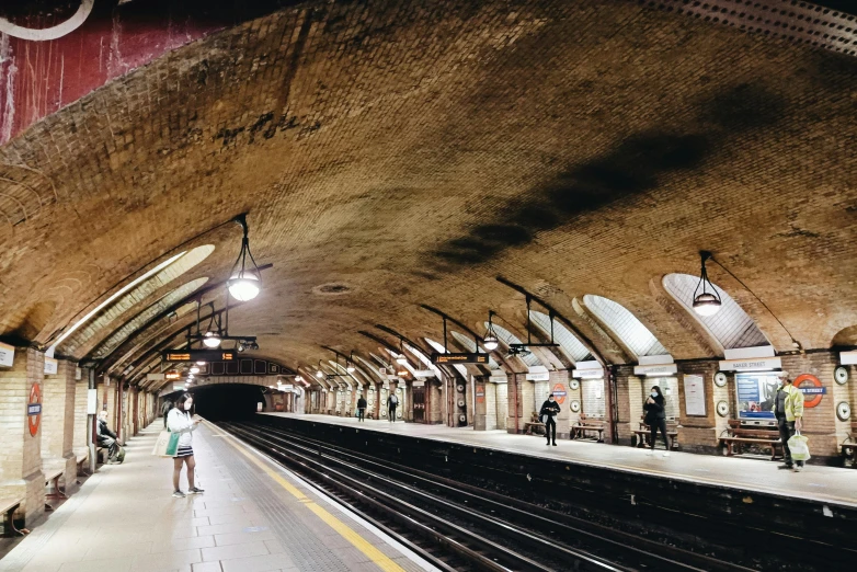 a train station with people standing on the platform, unsplash, art nouveau, down in the sewers of london, calm weather, 🚿🗝📝