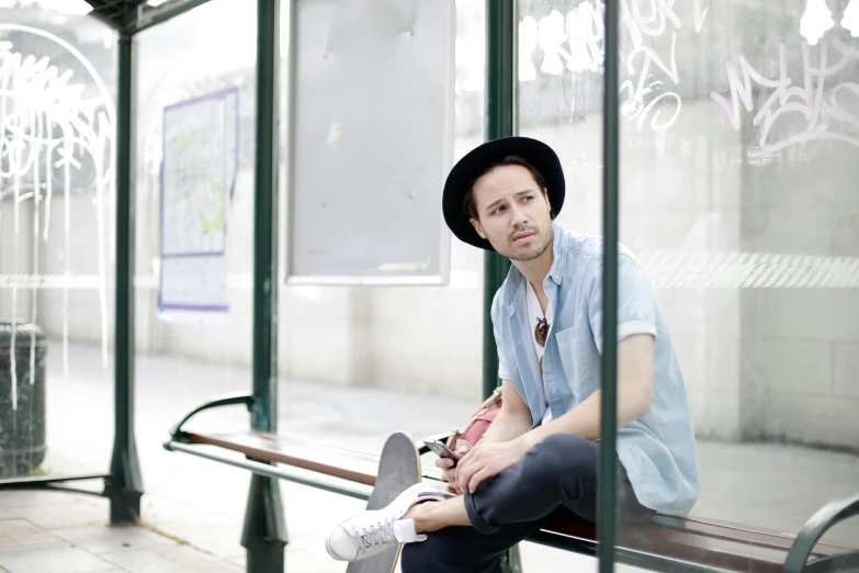 man in blue shirt and black hat sits on bench next to street