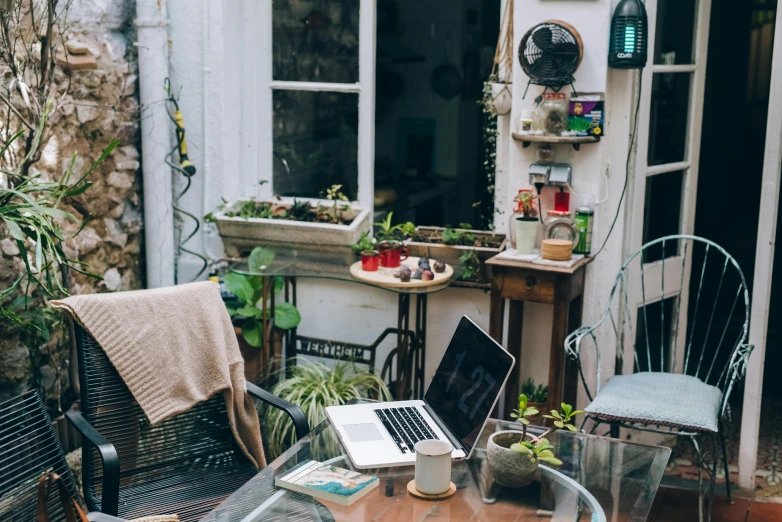 a laptop computer sitting on top of a glass table, by Romain brook, trending on pexels, maximalism, plants and patio, old apartment, small hipster coffee shop, built on a small