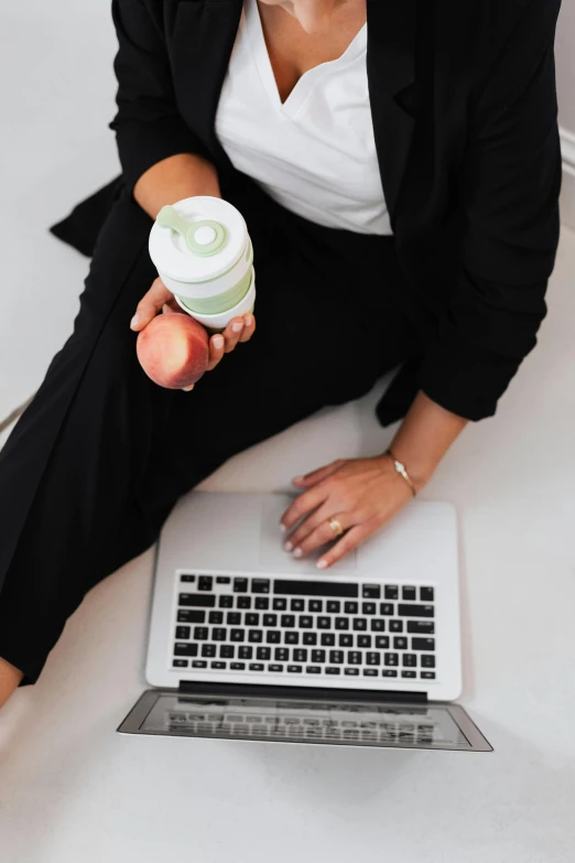 a woman sitting on a couch with a laptop and a cup of coffee, by Nicolette Macnamara, holding an apple, loputyn and matcha, peach, hip corporate