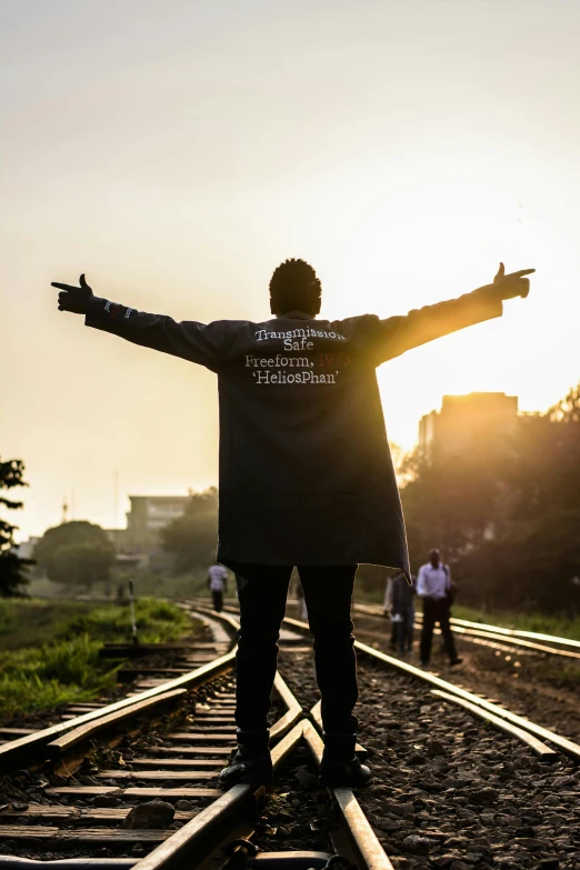 a man standing on a train track with his arms outstretched, an album cover, unsplash, happening, in sao paulo, praise the sun, waving robe movement, wearing track and field suit