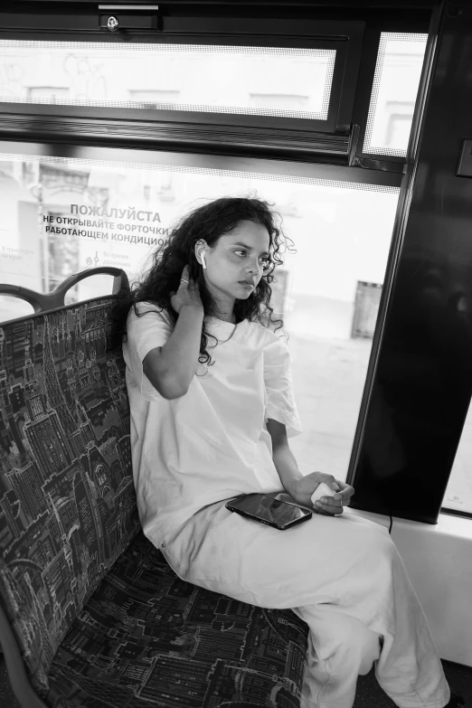 a woman sitting on a bus talking on a cell phone, a black and white photo, by Nathalie Rattner, nathalie emmanuel, фото девушка курит, white clothes, miro petrov