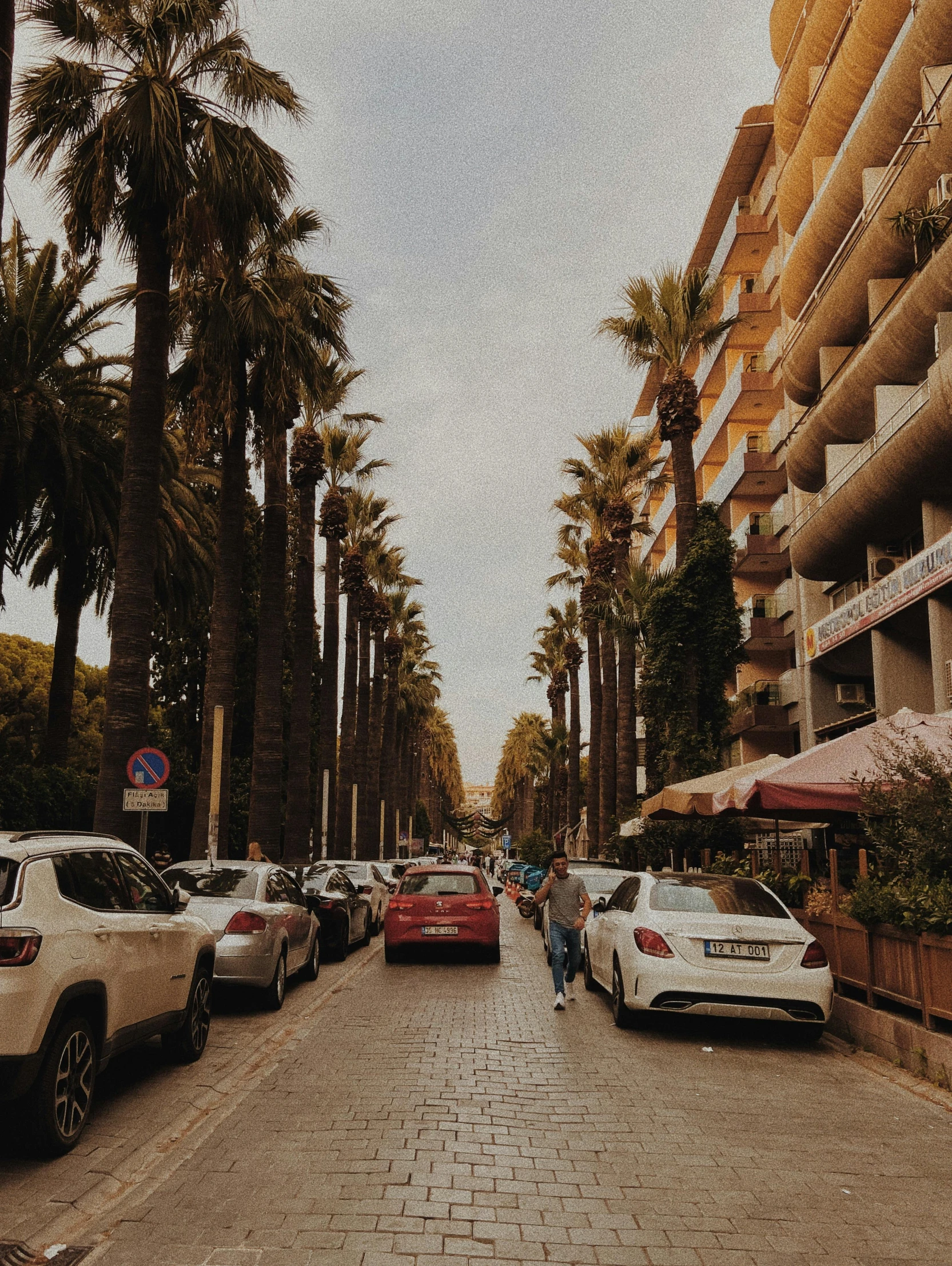 a street lined with parked cars and palm trees, by Alexis Grimou, pexels contest winner, cannes, profile image, people walking around, low quality photo