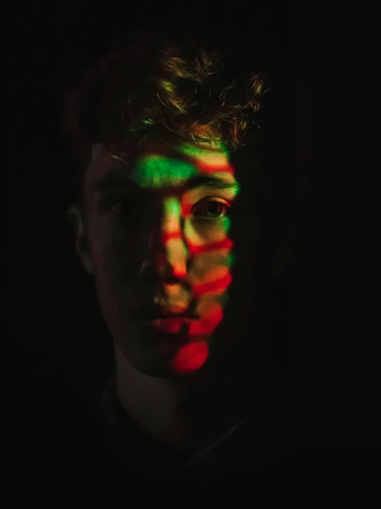 a close up of a person's face in the dark, an album cover, by Jacob Toorenvliet, pexels contest winner, holography, red haired teen boy, red and green, back light, multi colored
