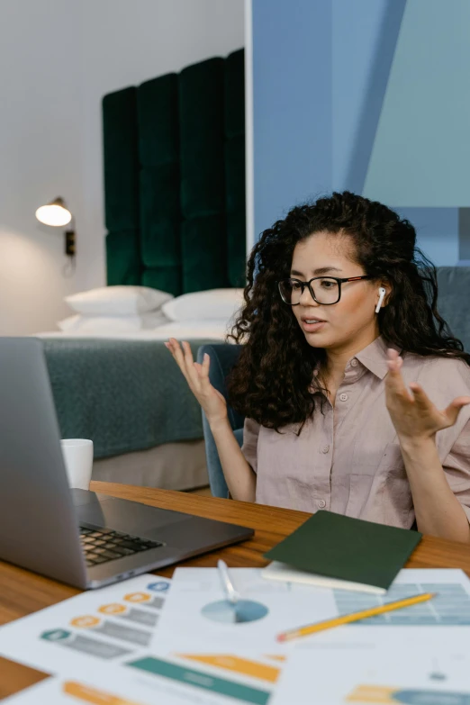 a woman sitting at a table in front of a laptop, shrugging, multiple stories, professional grade, wavy hair spread out