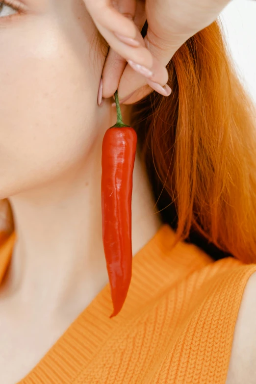a close up of a person wearing a pair of earrings, by Julia Pishtar, holding hot sauce, long nose, 165 cm tall, vegetable
