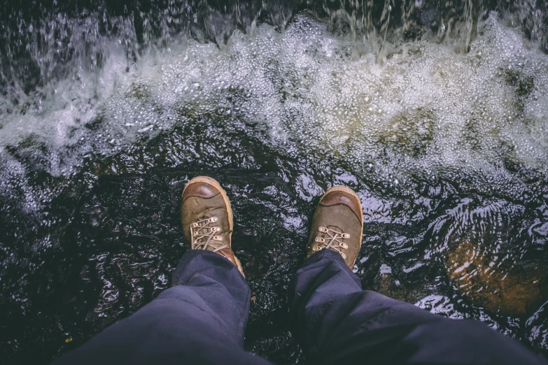 a person standing on a rock in the water, wearing boots, wild water, sitting on the floor, looking down from above
