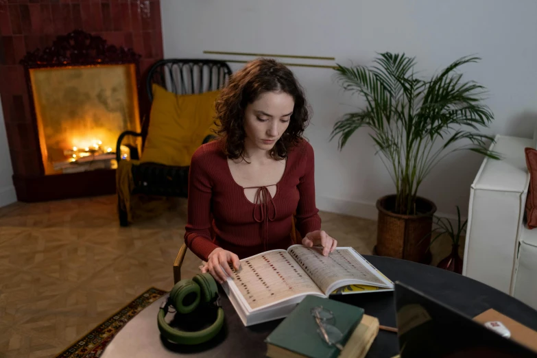 a woman sitting at a table reading a book, by Julia Pishtar, spell casting, textbooks and books, in a living room, promo image