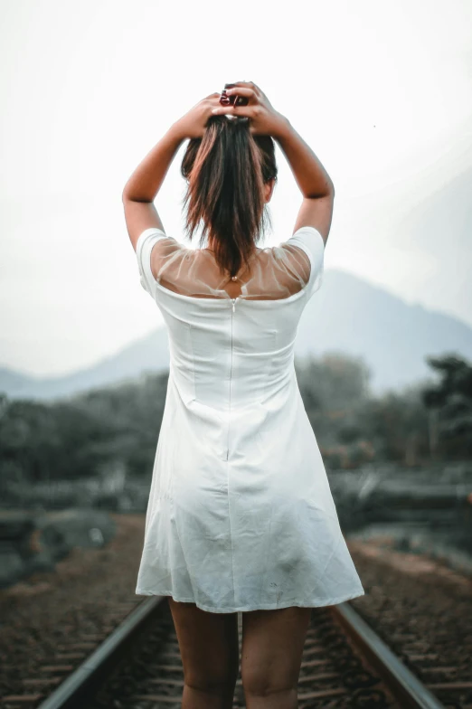 a woman in a white dress standing on a train track, pexels contest winner, renaissance, hands in her hair, indonesia, standing on a hill, arched back