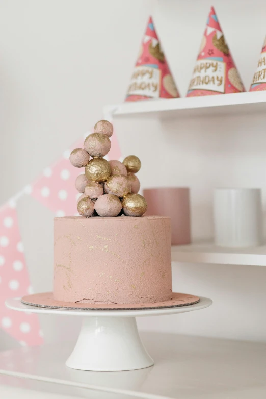 a pink cake sitting on top of a white cake plate, inspired by Anita Malfatti, unsplash, cups and balls, gold decorations, at a birthday party, grape