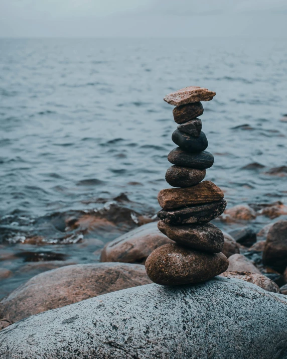 a stack of rocks sitting on top of a rock next to the ocean, in the middle of a lake, lgbtq, trending photo, tower