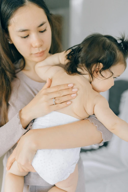 a woman holding a baby in her arms, trending on pexels, hunched shoulders, young asian girl, shiny soft skin, carefully crafted