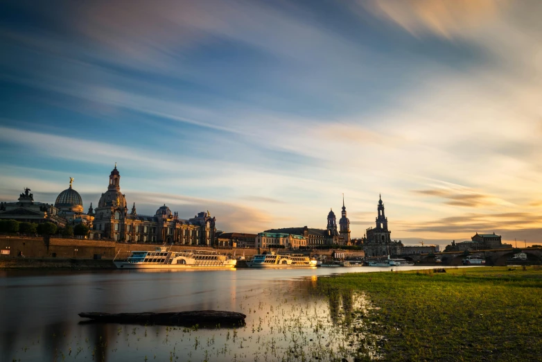 a large body of water next to a lush green field, a photo, by Sebastian Spreng, pexels contest winner, baroque, vista of a city at sunset, 3 boat in river, german renaissance architecture, docks