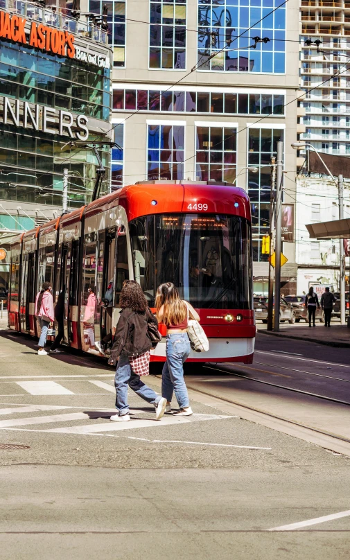a red bus driving down a street next to tall buildings, by Nicolette Macnamara, pexels contest winner, trams, toronto, people walking, north melbourne street