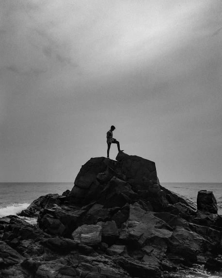 a person standing on top of a rock near the ocean, a black and white photo, by Adam Marczyński, unsplash contest winner, conceptual art, intimidating pose, strong silhouette, album cover, various posed