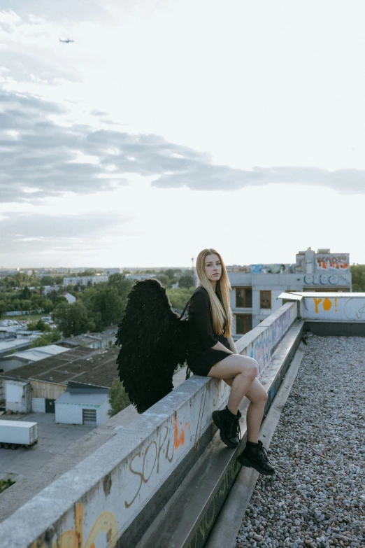 a woman sitting on a ledge on top of a building, black wings, anton fadeev 8 k, with long blond hair, full frame image