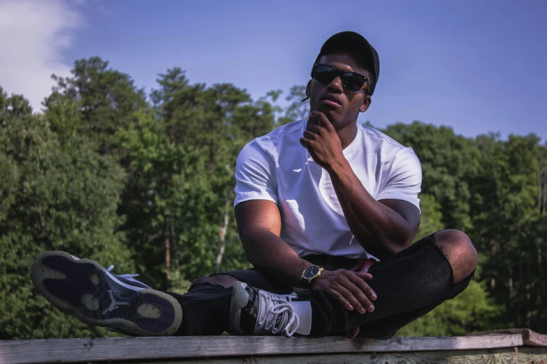 a man sitting on top of a wooden bench, dark skinned, profile image, sneaker photo, shades