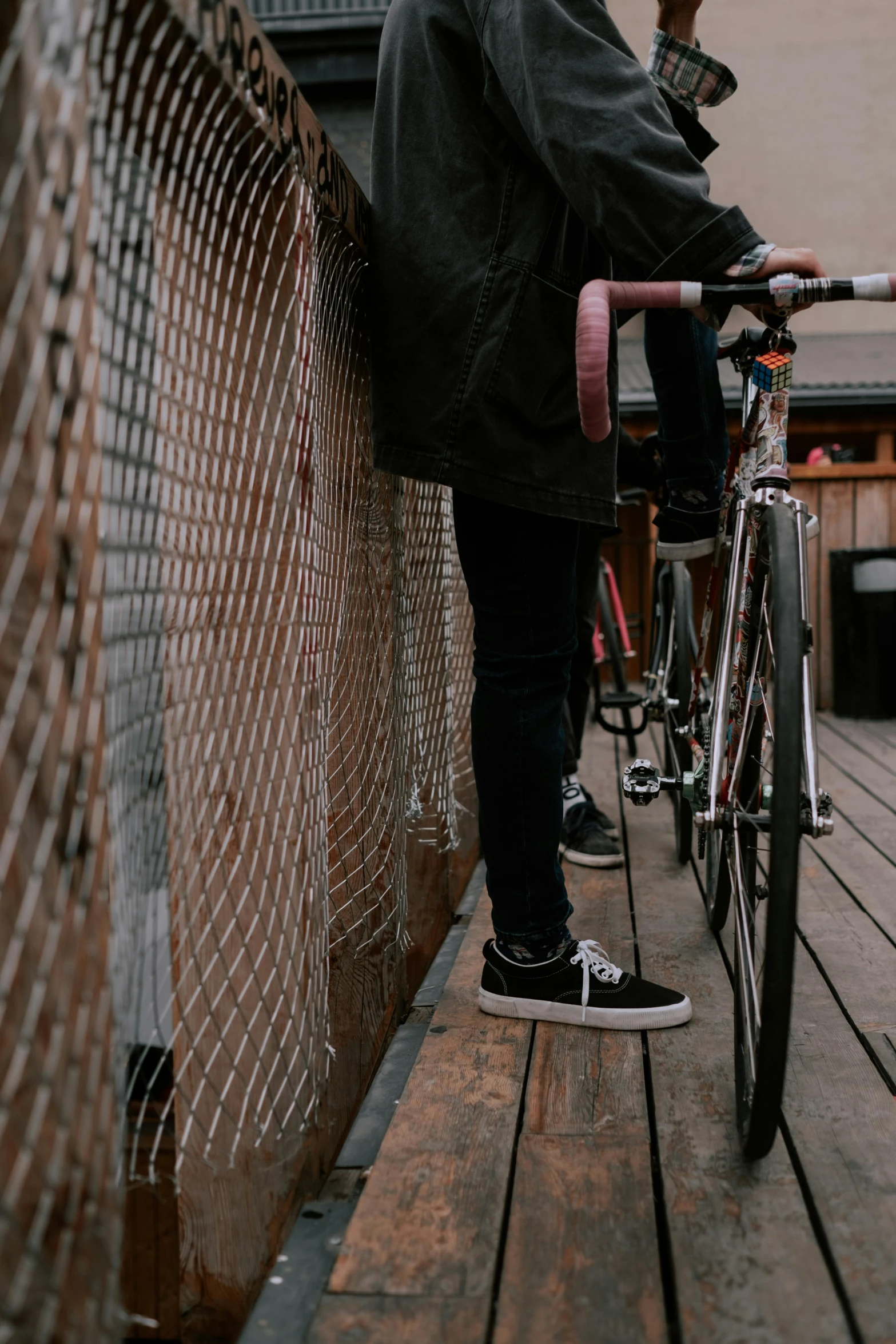 the girl in her black coat stands on the bridge while holding a bike