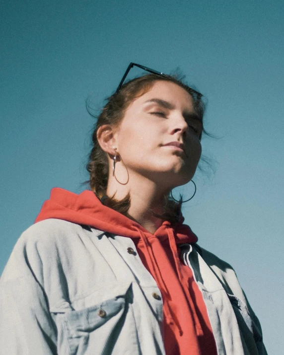 a woman standing in front of a blue sky, an album cover, by Grace Polit, trending on unsplash, antipodeans, wearing a scarlet hoodie, portrait of barbara palvin, androgynous male, giant earrings