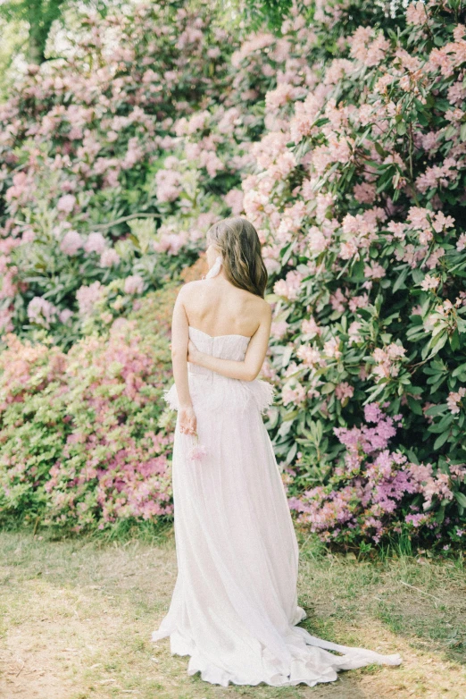 a woman standing in front of a bush of flowers, inspired by Oleg Oprisco, unsplash, wedding, back, high quality photo, white and pink