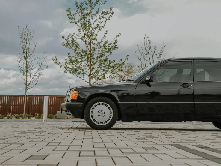 a black car parked in front of a wooden fence, by Matthias Stom, unsplash, mercedez benz, 80s nostalgia, on the concrete ground, profile image