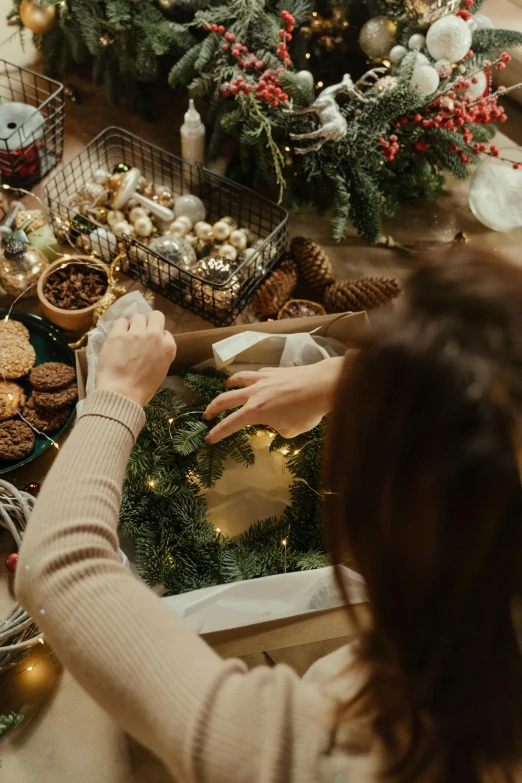 a woman sitting at a table in front of a christmas tree, crafting, ornamental halo, flatlay, brightly lit!